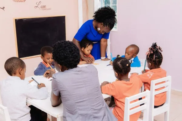A teacher helping young children draw together around a classroom table