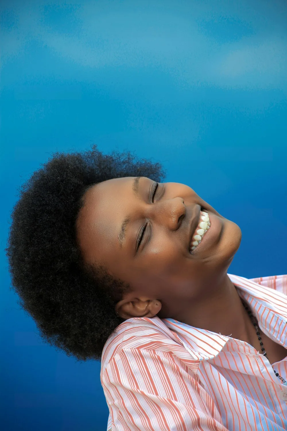 A woman smiling with her eyes closed against a bright blue background